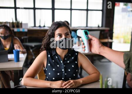 Businesswoman with face mask working indoors in office, measuring temperature. Stock Photo