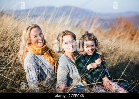 Small girl with mother and grandmother resting in autumn nature. Stock Photo