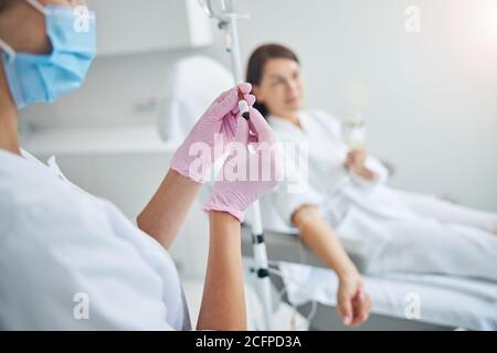Woman in latex gloves looking at an ampule in her hands Stock Photo