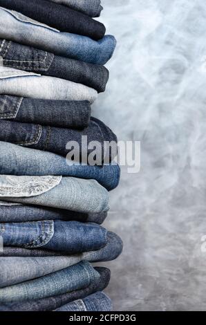 Stack of carelessly folded jeans on gray background. Close-up of jeans in different colors. Jeans texture or denim background. Copy space Stock Photo