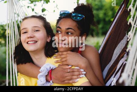 Front view of young teenager girls friends outdoors in garden, resting.