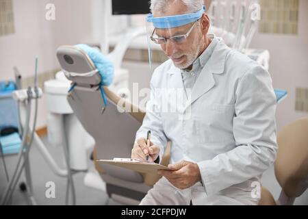 Busy dentist taking notes while sitting in his office Stock Photo