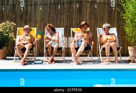 Group of cheerful seniors sitting by swimming pool outdoors in backyard. Stock Photo