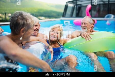 Group of cheerful seniors in swimming pool outdoors in backyard, talking. Stock Photo