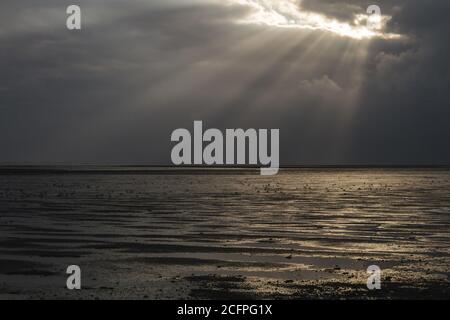 Dutch Wadden Isle Schiermonnikoog, sun beams shining through the clouds over the mud flats of the Wadden Sea during low tide, Netherlands, Stock Photo