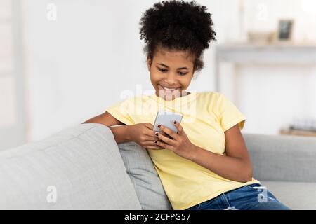 Happy Teen Girl Using Phone Sitting On Sofa At Home Stock Photo