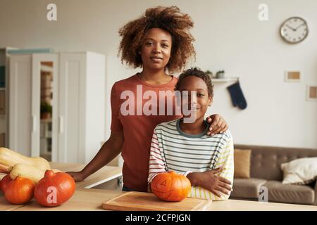Beautiful African American woman and her teen son standing together at table with pumpkins for carving on it Stock Photo