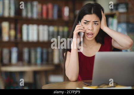 Frustrated asian woman having computer problems, talking on cellphone with customer support Stock Photo
