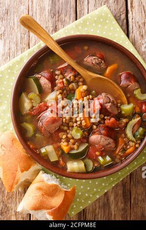 Homemade lentil soup with sausages and vegetables close-up in a plate on the table. vertical top view from above Stock Photo