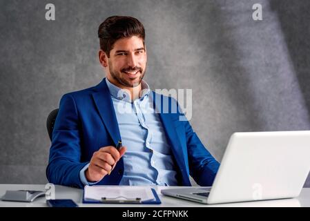 Cropped shot of happy businessman sitting behind his laptop and looking at camera while working in the office. Stock Photo