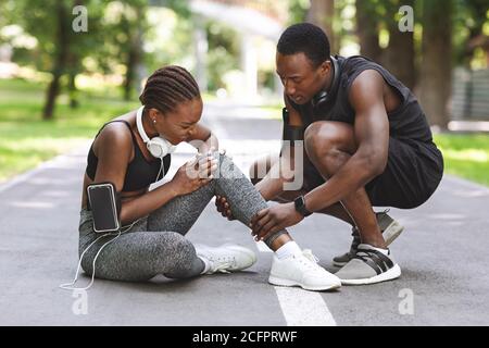 Sport Injury. Woman Suffering From Knee Trauma While Jogging With Boyfriend Outdoors Stock Photo