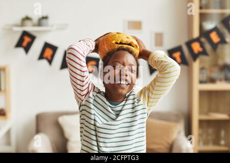 Playful African American boy having fun with Jack O' Lantern pumpkin putting it on his head, medium portrait shot Stock Photo
