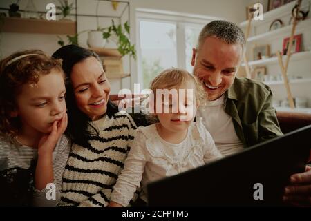 Portrait of excited happy family with children looking at a laptop at home relaxing on the couch relaxing - family bonding time Stock Photo