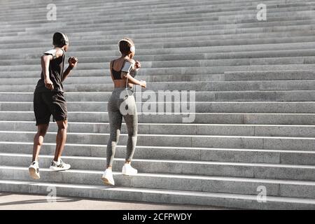 Couple Of Sporty Black Joggers Running Up The Steps In Urban Park Stock Photo