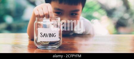 Happy asian children saving money putting coin in glass for wealth and growth of earning, finance and investment for success, boy planning and deposit Stock Photo