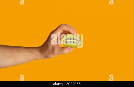 Male hand holding cut ripe kiwi fruit over orange background Stock Photo
