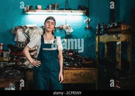 The concept of small business, feminism and women's equality. A young woman in working clothes posing in front of an auto shop. Stock Photo