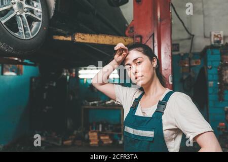 Gender equality. A young brunette in uniform stands near the Elevator with a car and wipes the sweat from her forehead. In the background is an auto r