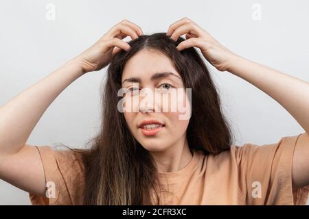 Dandruff and lice. Portrait of a young Caucasian woman, a brunette, who strongly scratches her head with her hands. White background. Stock Photo