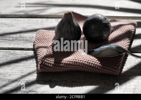ripe figs beautifully arranged on a white shabby chic wooden table on an old pink napkin, hard shadows of a palm Stock Photo