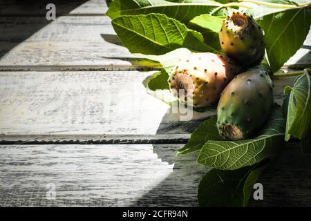 prickly pears nicely arranged on a white shabby chic wooden table with fig leaves, flat lay Stock Photo
