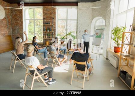 Male speaker giving presentation in hall at university workshop. Audience or conference hall. Young students, participants in audience wearing face mask. Scientific conference event, training. Education Stock Photo