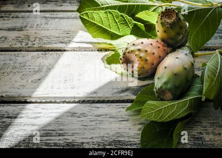 prickly pears nicely arranged on a white shabby chic wooden table with fig leaves, flat lay Stock Photo