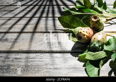 prickly pears nicely arranged on a white shabby chic wooden table with fig leaves, on the background a shadow of a palm, flat lay Stock Photo