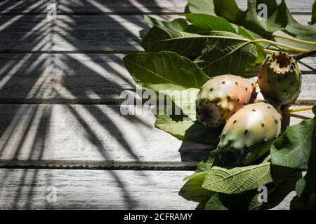 prickly pears nicely arranged on a white shabby chic wooden table with fig leaves , on the background a shadow of a palm, flat lay Stock Photo