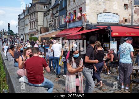 female with smartphone and other tourists wearing face masks during the COVID-19 pandemic in the picturesque harbour town of Honfleur in Normandy Stock Photo