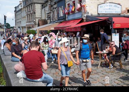 Couple holding hands and other tourists wearing face masks during the COVID-19 pandemic in the picturesque harbour town of Honfleur in Normandy Stock Photo