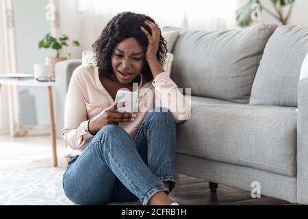 Bad News. Upset Shocked African Woman Reading Message On Smartphone At Home Stock Photo