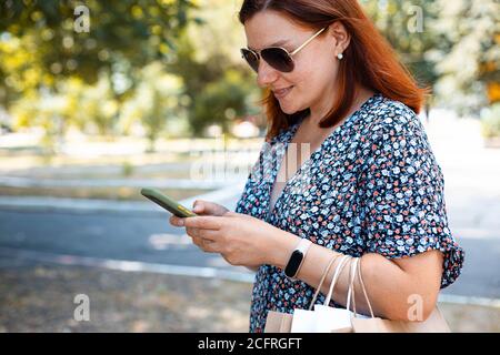 Woman using smartphone with shopping bags in hands in the park on a sunny day. Shopping concept Stock Photo