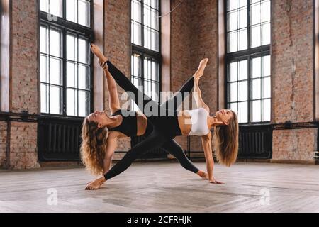 Star shape acrobatic composition made from two woman bodies in big loft room. Stock Photo