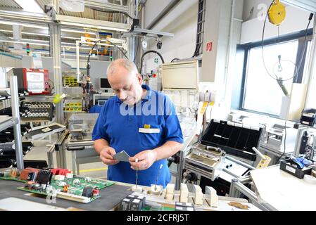 older friendly worker in an industrial company assembles electronic components in the mechanical engineering of a modern factory Stock Photo