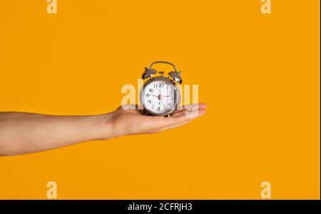Time management and deadline. Millennial guy holding alarm clock over orange background, closeup Stock Photo