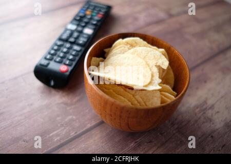 bowl of chips and tv remote on wooden background . Stock Photo