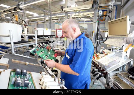 older friendly worker in an industrial company assembles electronic components in the mechanical engineering of a modern factory Stock Photo