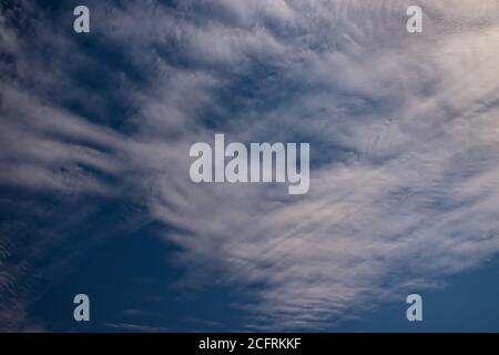 Thin cirrus clouds, blowing in the whirlwind winds, under a navy blue sky. Stock Photo