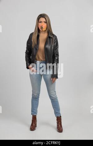 latin woman with colorful mask and leather jacket, standing front, studio photo with gray background Stock Photo