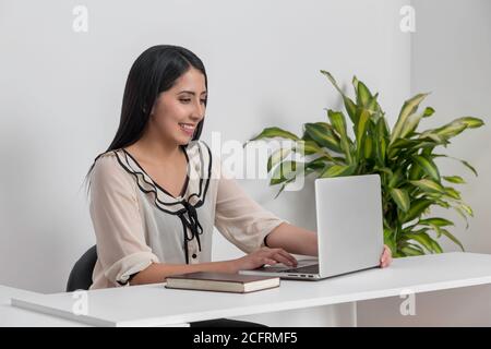 young female professional working on laptop, smiling with white blouse Stock Photo