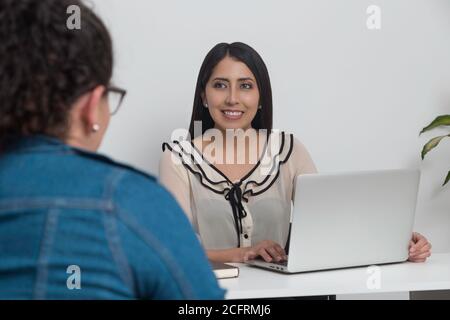 female doctor talking to her patient with a laptop on his desk, office with white wall Stock Photo