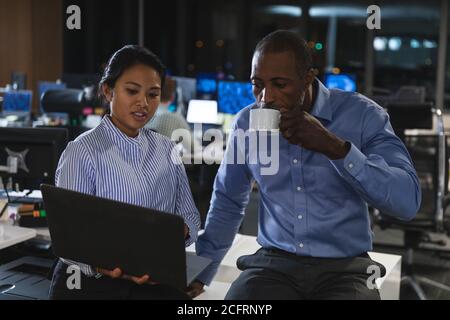 Senior businessman drinking coffee while discussing with young businesswoman over laptop Stock Photo