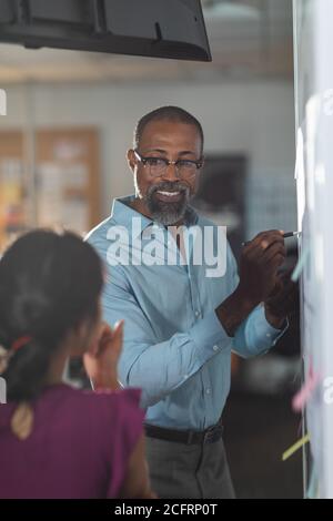 Senior businessman wearing glasses writing on white board in modern office Stock Photo