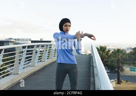 Woman in hijab performing stretching exercise on a footbridge Stock Photo