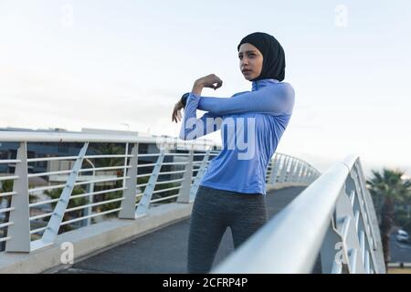 Woman in hijab performing stretching exercise on a footbridge Stock Photo