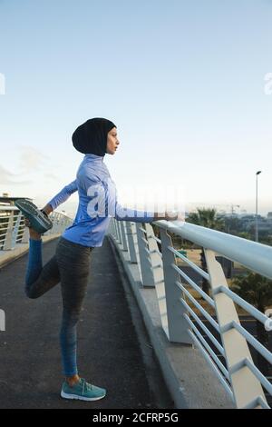 Woman in hijab performing stretching exercise on a footbridge Stock Photo