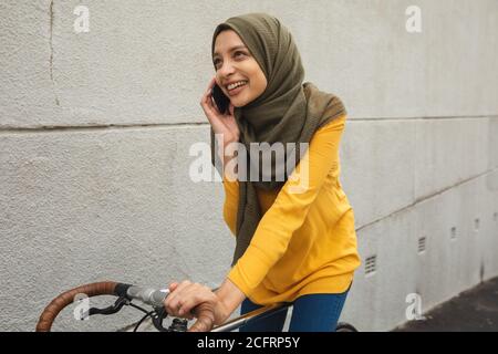 Woman in hijab talking on smartphone while riding bicycle Stock Photo