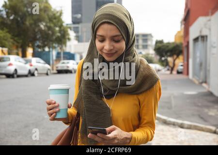 Woman in hijab with coffee cup using smartphone on the street Stock Photo