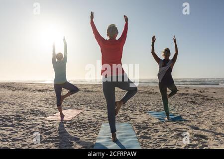 Rear view of group of woman practicing yoga on the beach Stock Photo